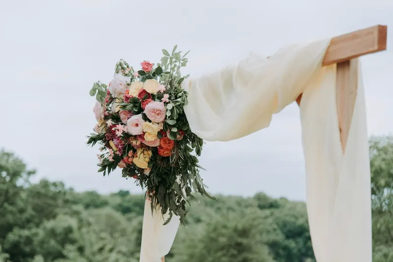 A wedding arch draped in ivory fabric with a bouquet of flowers